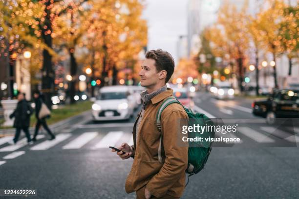 man crossing the street, holding a smartphone. - man side way looking stock pictures, royalty-free photos & images