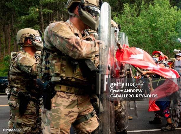 Protester hits the shields of National Guard troops as they block the road to Mount Rushmore National Monument with vans as they protest and confront...