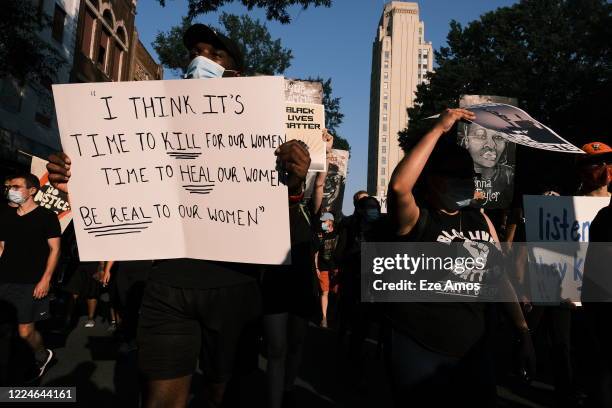 Protester carries a sign that quotes Tupac Shakur and reads "I think its time to kill for our women, Time to heal our women, Be real to our women"...