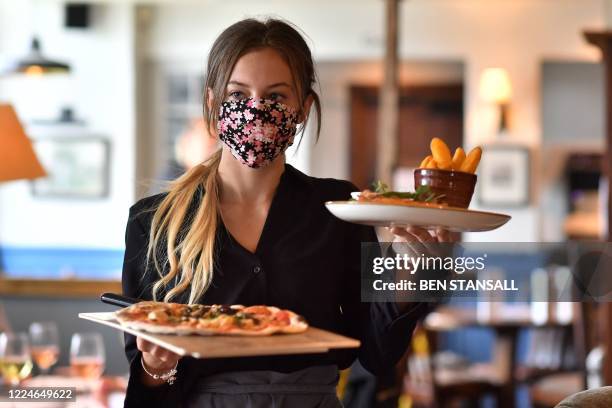 Staff member wears a face mask as she serves customers at the The Shy Horse pub and restaurant in Chessington, Greater London on July 4 on the first...