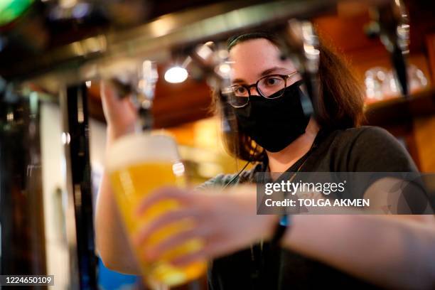 Member of bar staff wearing PPE in the form of a face mask, pours drinks inside the Wetherspoon pub, Goldengrove in Stratford in east London on July...