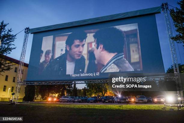 People in their cars watch a movie "Grease" with John Travolta and Olivia Newton-John at a temporary drive-in cinema parking lot. Due to the spread...