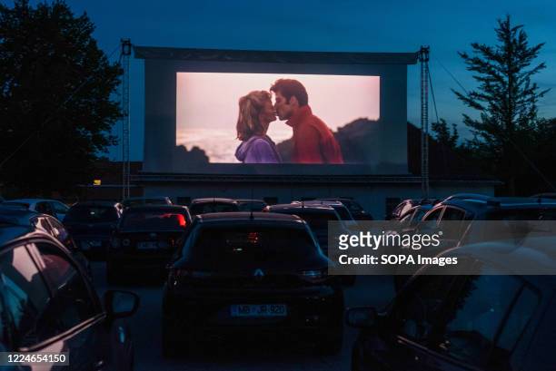 People in their cars watch a movie "Grease" with John Travolta and Olivia Newton-John at a temporary drive-in cinema parking lot. Due to the spread...
