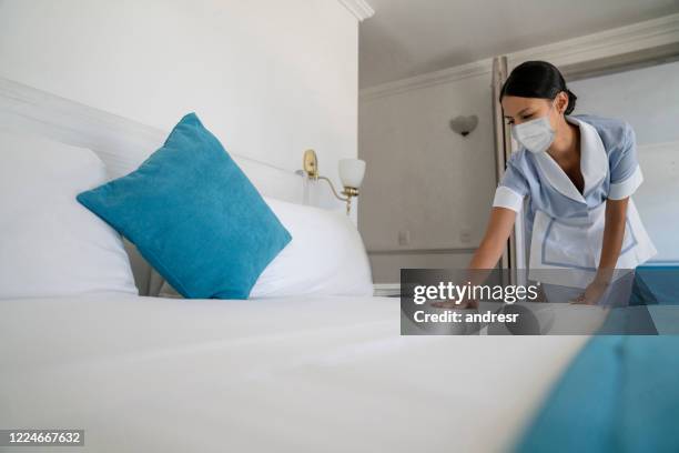 maid doing the bed wearing a facemask while working at a hotel - blue collar worker mask stock pictures, royalty-free photos & images