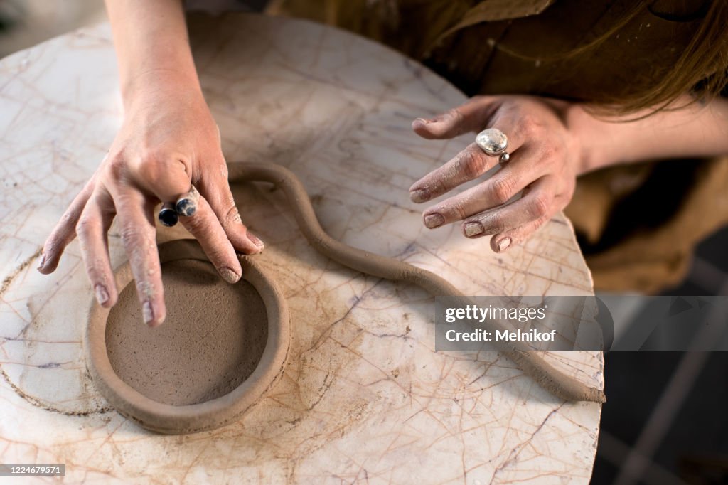 Crop potter making coil vessel on marble table in workshop