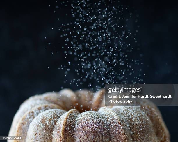 studio shot of the top half of a bundt cake with powdered sugar falling down - powdered sugar stock-fotos und bilder