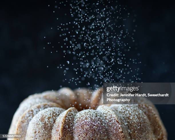 studio shot of the top half of a bundt cake with powdered sugar falling down - pastel bundt fotografías e imágenes de stock