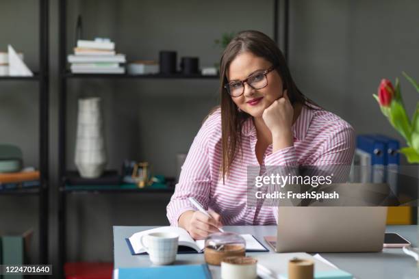 portrait of a confident businesswoman sitting at her office, looking at camera - pink shirt stock pictures, royalty-free photos & images