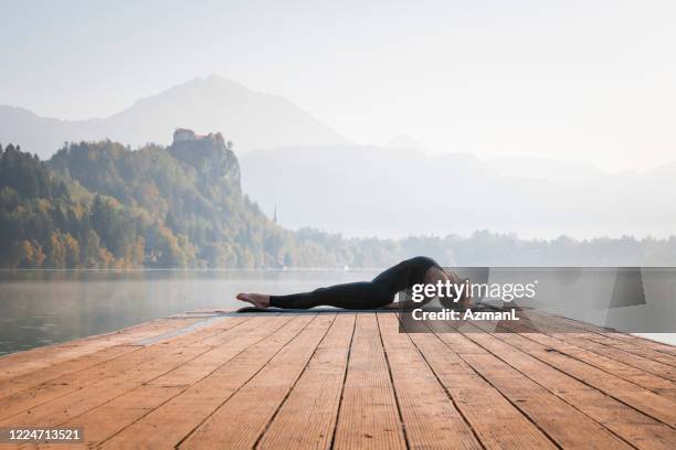 woman in yoga fish posture on pier overlooking lake bled - fish pose stock pictures, royalty-free photos & images