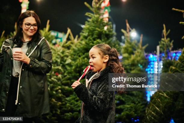 young girl eating candy cane while shopping for christmas tree with family - african people buying a christmas tree stockfoto's en -beelden