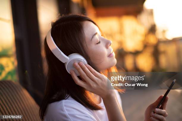 close-up shot of young woman enjoying music over headphones and using smart phone - listening stockfoto's en -beelden