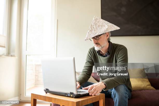 man (age 51) using laptop while wearing a tinfoil hat - aluhut 個照片及圖片檔