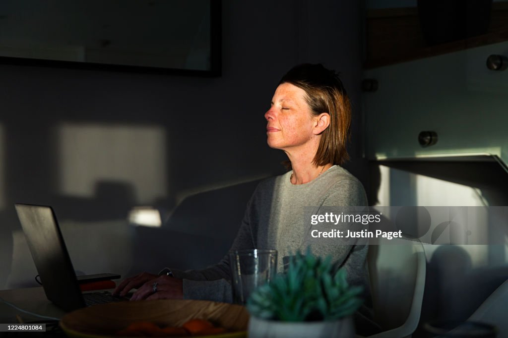 Woman closing her eyes as the last sun rays of the day come into her house