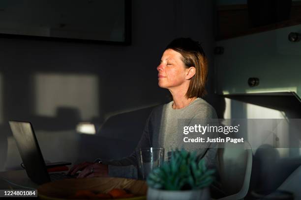 woman closing her eyes as the last sun rays of the day come into her house - benessere mentale foto e immagini stock