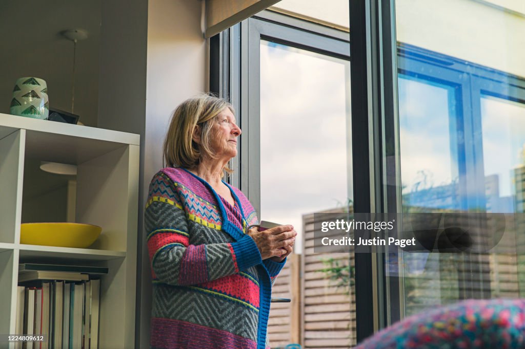 Senior woman looking out of window with a cuppa