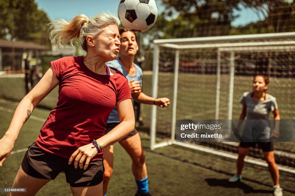 Female soccer striker heads ball into the goal