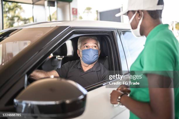 gas station attendant talking to customer at car at service station - with face mask - gas station attendant stock pictures, royalty-free photos & images