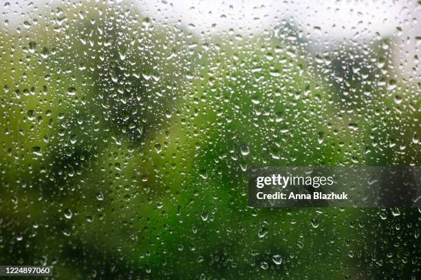 close up of rain drops on window on the rainy day, blurred green trees in background - raindrop stock pictures, royalty-free photos & images