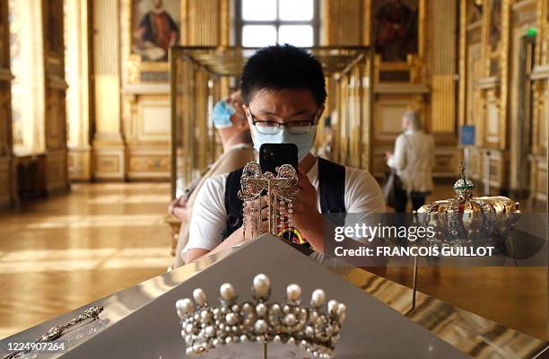 Visitor wearing face mask takes a pictures of Empress Eugenie's jewelry piece composed of "Grand noeud de corsage de l'Impératrice Eugénie" and the...