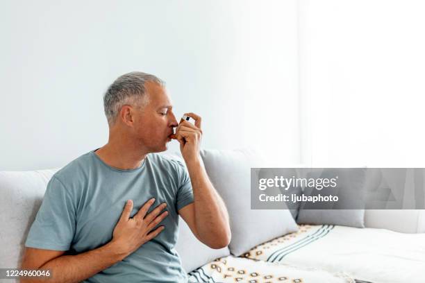 hombre maduro usando inhalador de asma - asmático fotografías e imágenes de stock