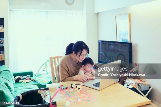 mother multi-tasking with infant daughter in home kitchen - mother and baby and laptop stock pictures, royalty-free photos & images