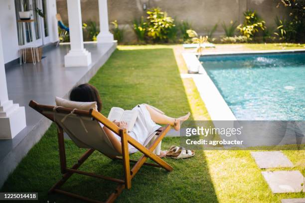 vrouw met zonnebril die een boek naast het zwembad gebruikt - protection luxe stockfoto's en -beelden