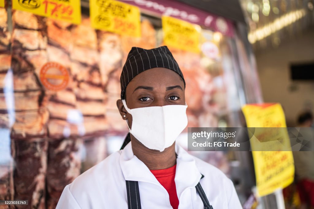 Retrato de carnicero femenino trabajando en la carnicería - con máscara facial