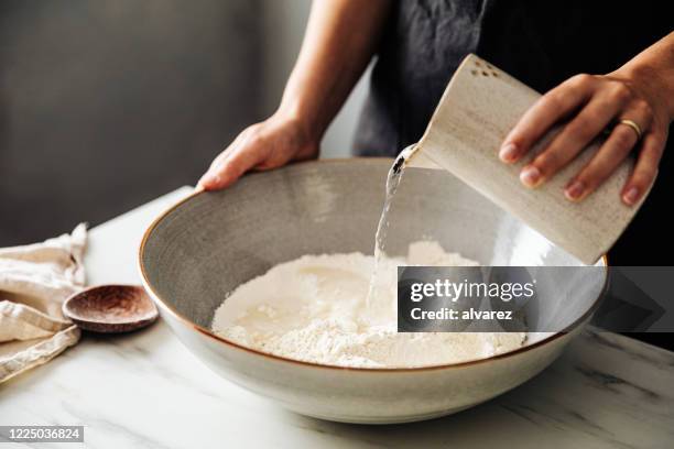 mujer vertiendo agua sobre harina de centeno y trigo en un tazón - cooking pan fotografías e imágenes de stock