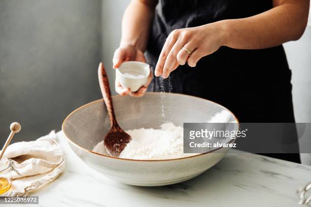 woman sprinkling salt in flour before mixing - food staple stock pictures, royalty-free photos & images