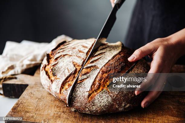 frau schneidet sauerteigbrot mit messer an bord - backwaren stock-fotos und bilder