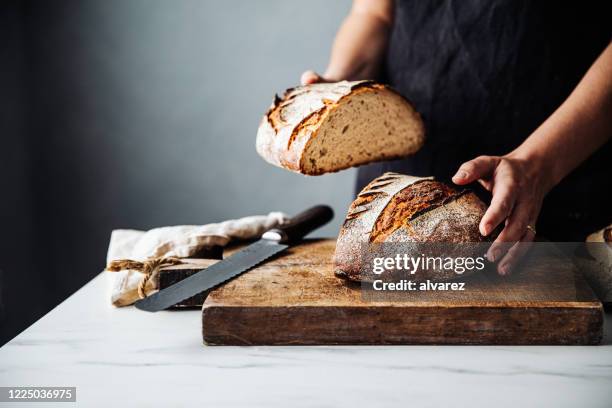 donna che tiene il pane sul tagliere in cucina - pane a lievito naturale foto e immagini stock