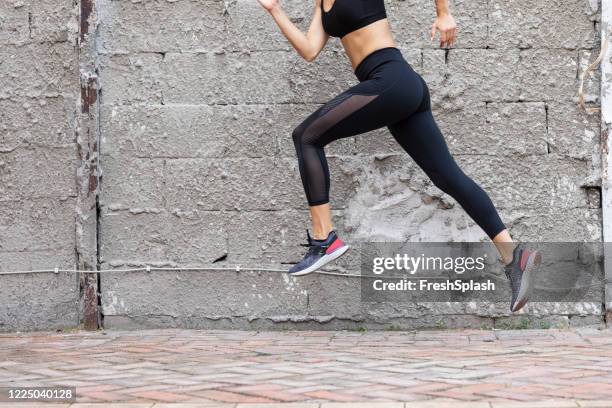 fit woman in black sportswear running outdoors - pantalón gris fotografías e imágenes de stock