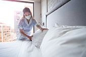 Maid working at a hotel and doing the bed wearing a facemask