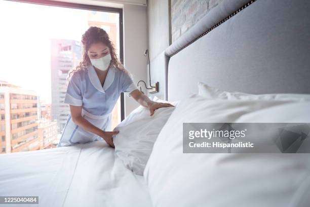 maid working at a hotel and doing the bed wearing a facemask - hotel stock pictures, royalty-free photos & images
