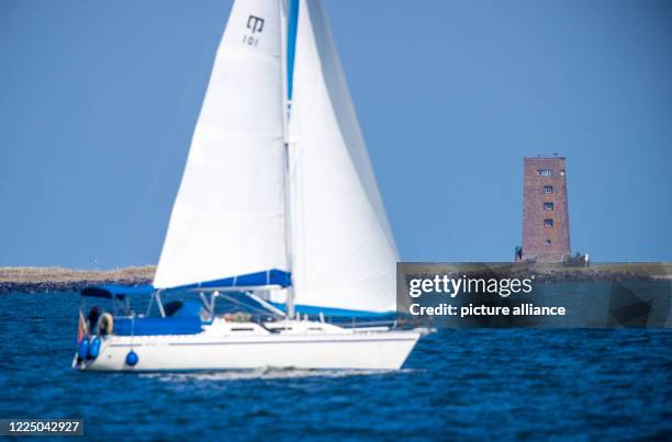 July 2020, Mecklenburg-Western Pomerania, Ruden: A sailing boat passes the Baltic Sea island Ruden with the measuring tower Station 19 in the...