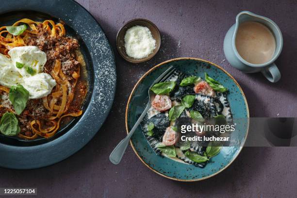 traditional italian dishes for family dinner. fettuccini bolognese with buffalo mozzarella and crab ravioli nero - squid ink pasta stock pictures, royalty-free photos & images