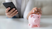 Woman saving money using smartphone and piggy bank