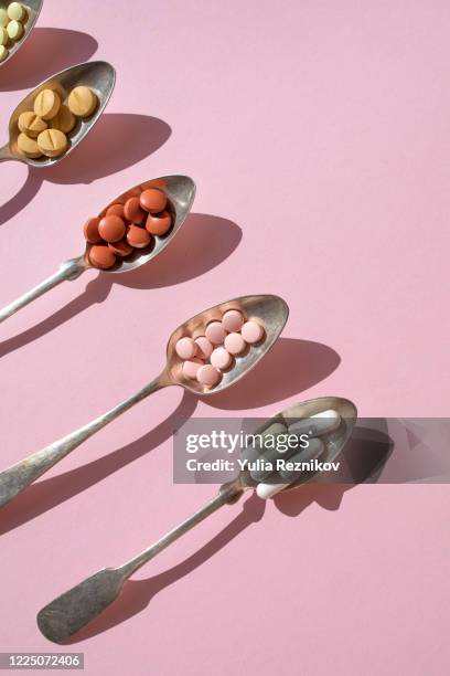 various of spoons with pills and tablets on the pink background - nahrungsergänzungsmittel stock-fotos und bilder