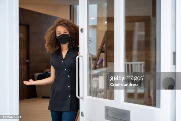 business owner opening the door of her spa wearing a facemask - opening event stock pictures, royalty-free photos & images