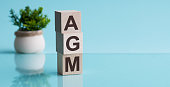AGM - Annual general meeting - acronym on wooden cubes on blue backround. Business concept.