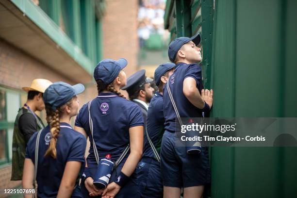 July 06: Ball boys and ball girls watching play through gaps in the stadiums doorways as they wait to work on Court Eighteen during the Wimbledon...