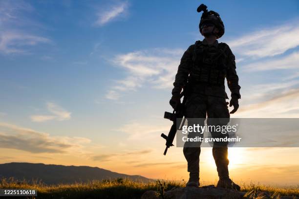 silhouette of standing soldier in battlefield at sunset - soldado do exercito imagens e fotografias de stock