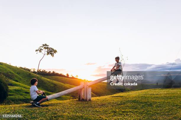 zwei kinder spielen auf wippe im freien bei sonnenuntergang - wippe stock-fotos und bilder