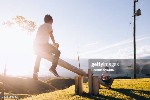 two kid playing on seesaw outdoors during sunset - seesaw stock pictures, royalty-free photos & images
