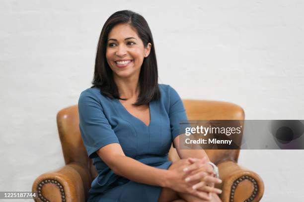 bright smiling hispanic woman relaxing on leather chair - woman excited sitting chair stock pictures, royalty-free photos & images