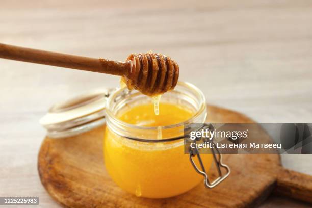 honey dripping from a wooden dipper in jar on old cutting board on white wooden rustic background - taste for a cure stock pictures, royalty-free photos & images