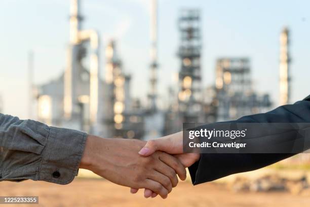 two business persons shaking hands over oil refinery plant of petroleum. - contract manufacturing stock pictures, royalty-free photos & images