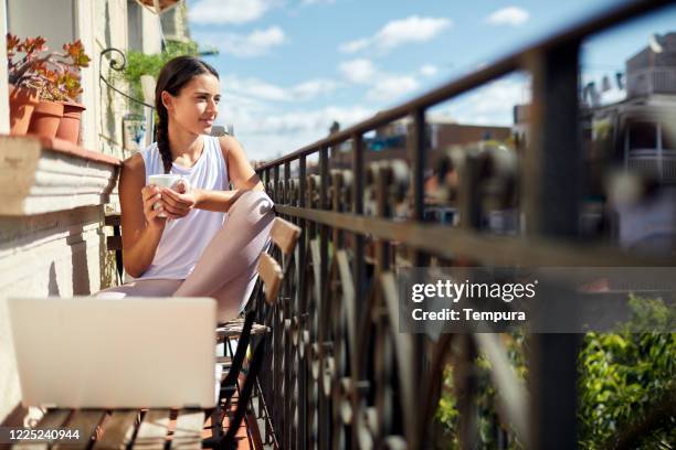 één jonge vrouwenzitting bij het balkon en houdend een kop koffie - italiaanse etniciteit stockfoto's en -beelden