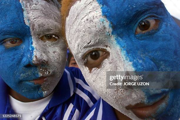 Two fans with the colors of the Guatemalan flag painted on their faces look into the camera, in front of the Carlos Salazar Stadium in Mazatenango,...