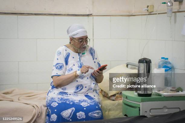 July 2020, Egypt, Giza: A coronavirus patient breathing through an oxygen mask, uses her mobile phone at a ward in the 6th of October Central...